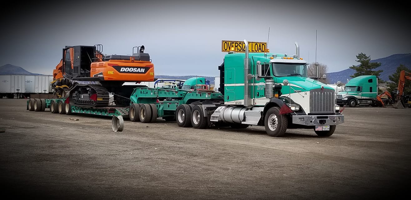 Western Heavy Haul oversize-load truck hauling an excavator across Central Oregon